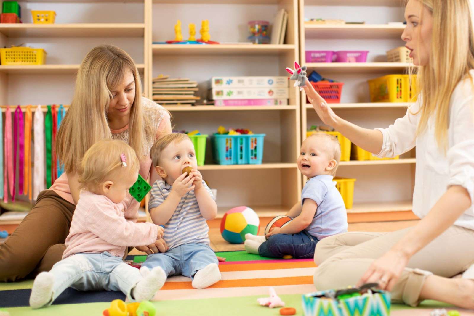 Group of babies in nursery. Nursery teacher and assistant play with kids